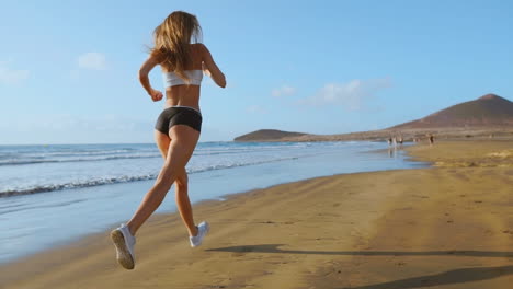 Beautiful-sporty-women-in-white-sneakers-running-along-a-beautiful-sandy-beach,-healthy-lifestyle.-Rear-view.-SLOW-MOTION-STEADICAM.